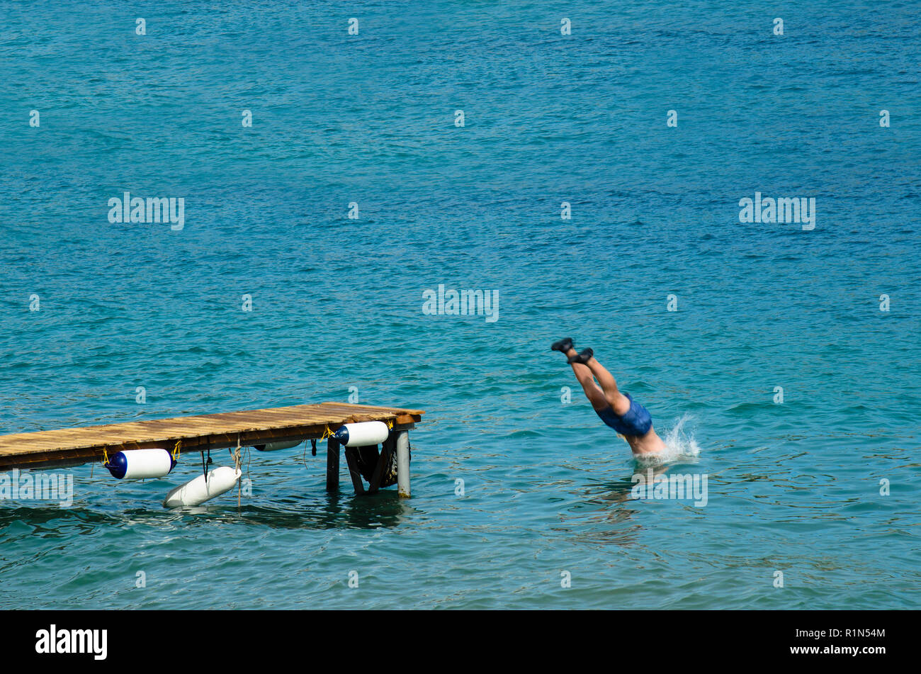 Uomo in un costume da bagno si tuffa nel mare da un molo in legno, vestita di nero scarpe di gomma Foto Stock