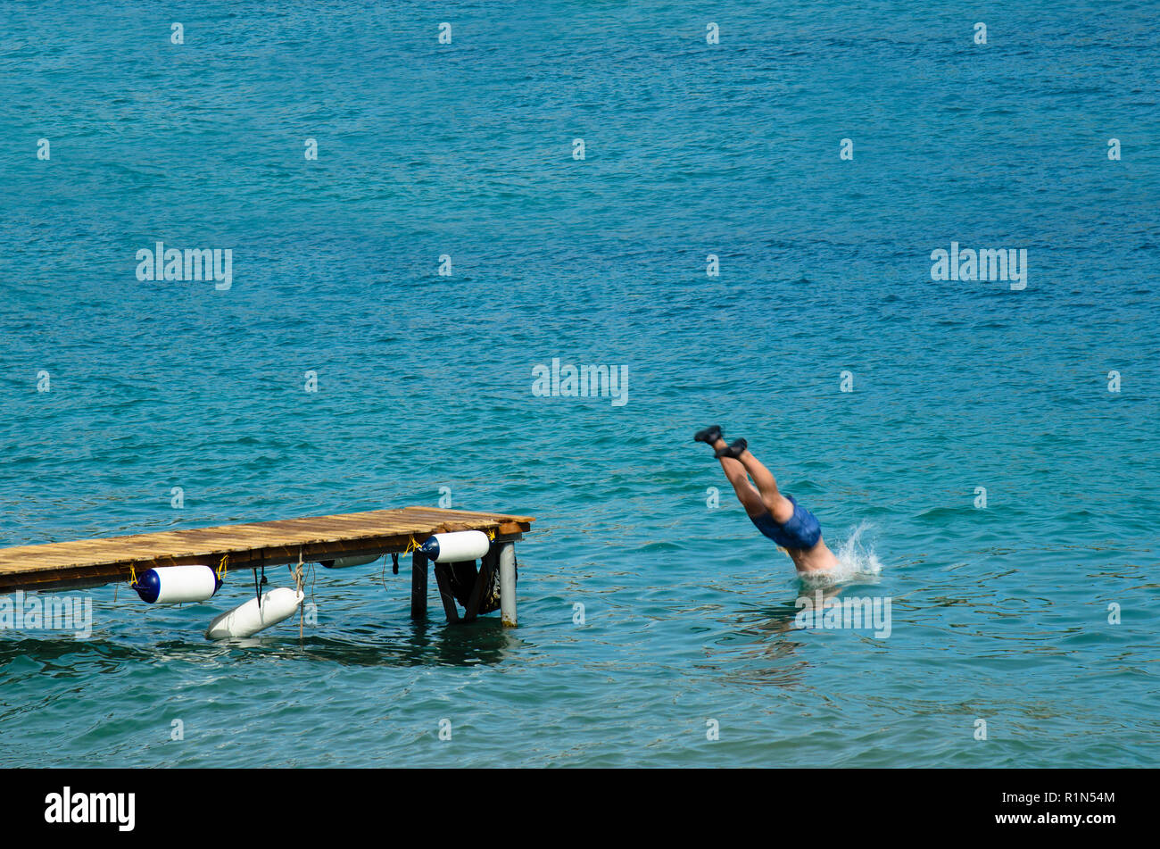 Uomo in un costume da bagno si tuffa nel mare da un molo in legno, vestita  di nero scarpe di gomma Foto stock - Alamy