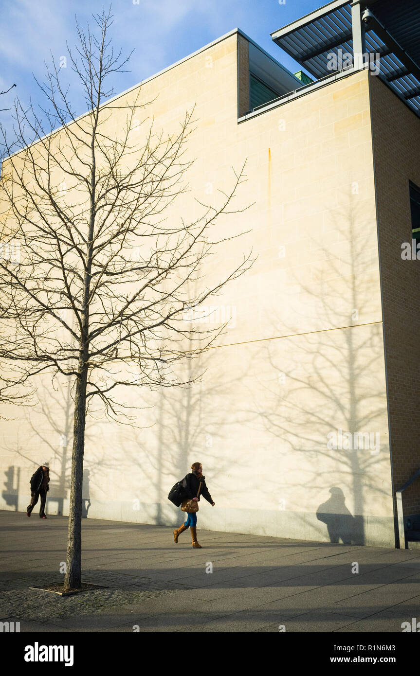 Due persone camminano oltre la Said Business School in Frideswide Square, Oxford, nel sole che getta ombre sul muro Foto Stock