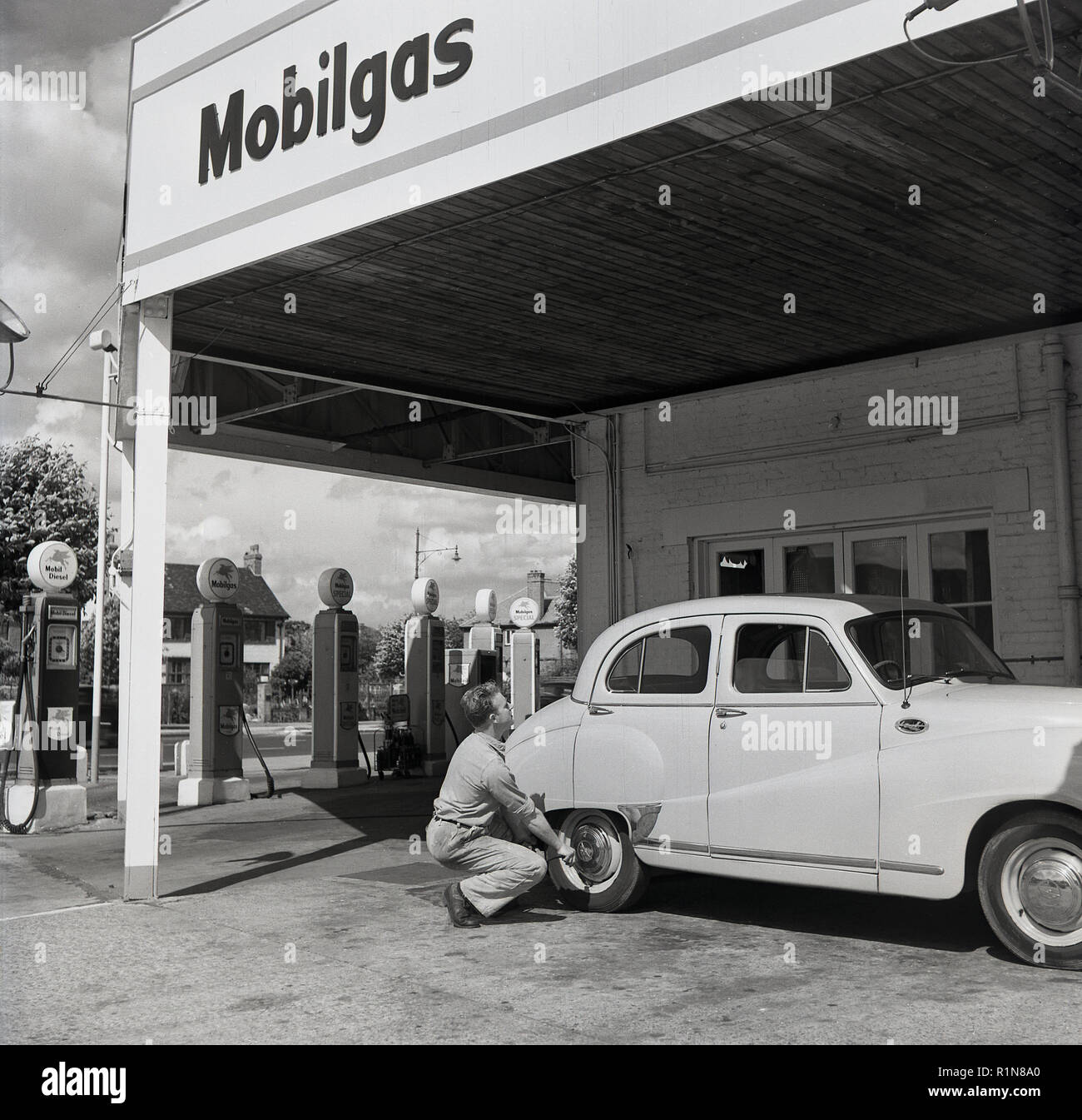 Degli anni Cinquanta, storico i giorni d'oro dell'automobilismo, una stazione di servizio sttendant controlla la pressione di gonfiaggio dei pneumatici su una Austin auto parcheggiate al Mobilgas Ravenscroft stazione di servizio, Great West Road, Londra, Inghilterra, Regno Unito. Foto Stock