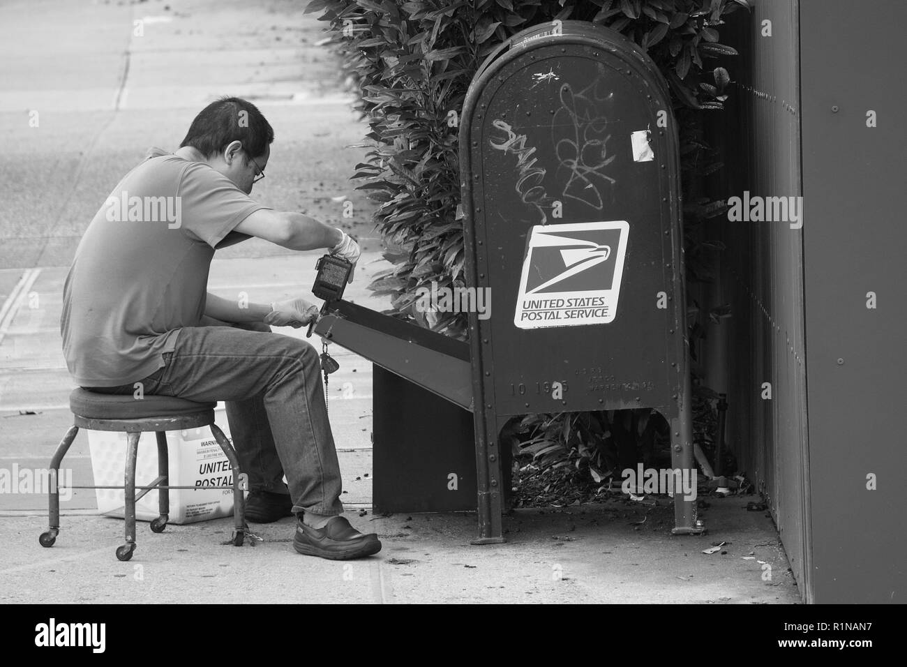 USPS postino seduto su strada la riparazione di una cassetta postale cycliner serratura. Foto Stock