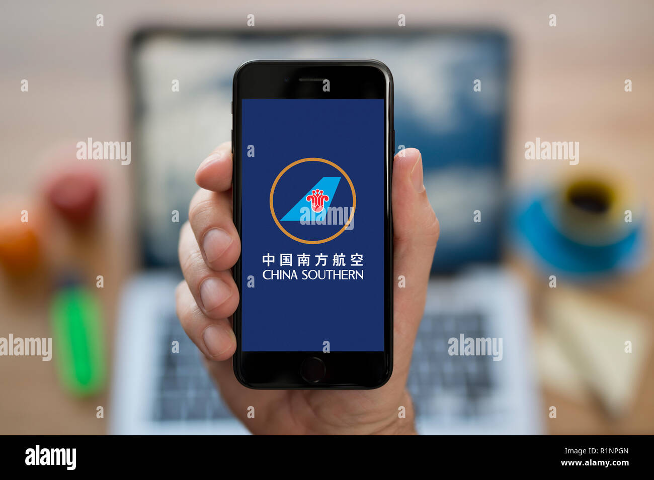 Un uomo guarda al suo iPhone che visualizza la China Southern Airlines logo, mentre se ne sta seduto alla sua scrivania per computer (solo uso editoriale). Foto Stock