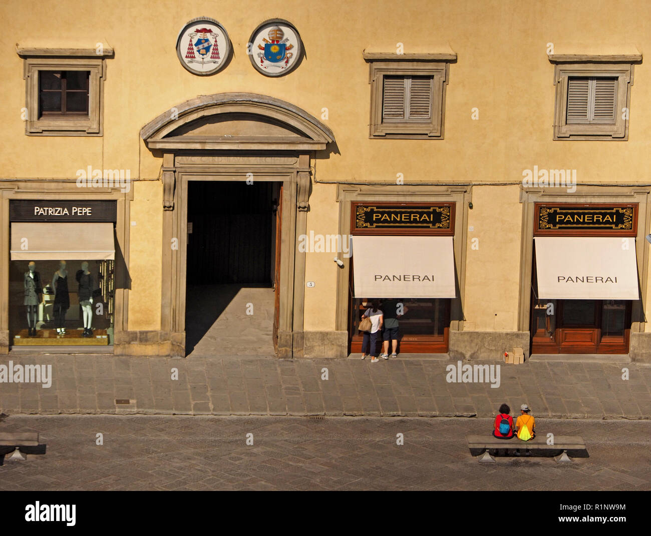 Due turisti vestito in abiti luminosi di sedersi su un banco di pietra nel normalmente occupato Piazza del Duomo Firenze,Toscana, Italia. un altro paio di window-shop Foto Stock