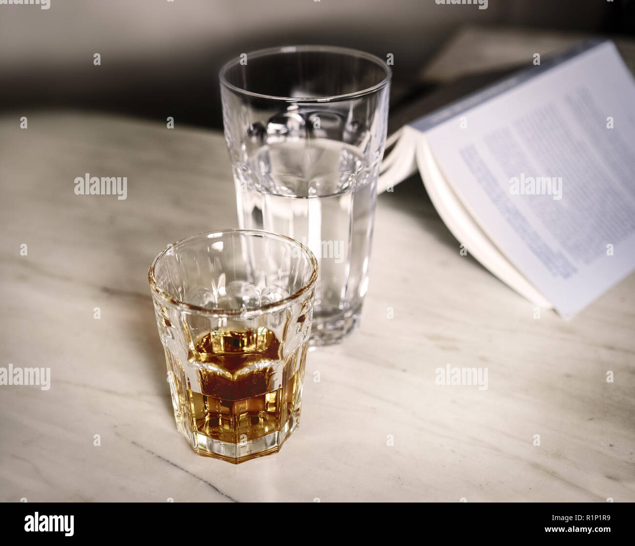 Un bicchiere di alcol, un bicchiere di acqua e un libro su un tavolo di marmo. Foto Stock