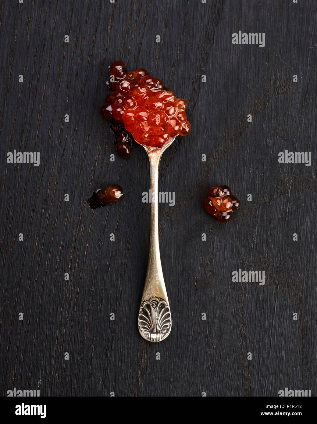Caviale rosso in un cucchiaio su nero lo sfondo di legno Foto Stock