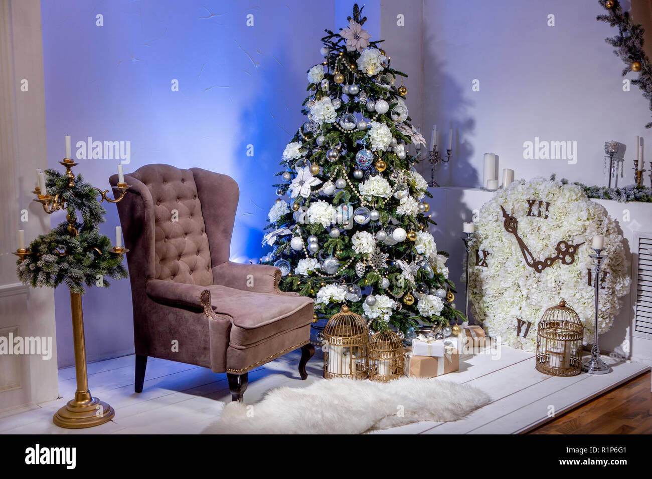 Natale camera decorata con poltrona marrone, grande orologio con fiori, candelabro con ghirlanda di abete e splendente albero di Natale con doni. Natale ev Foto Stock