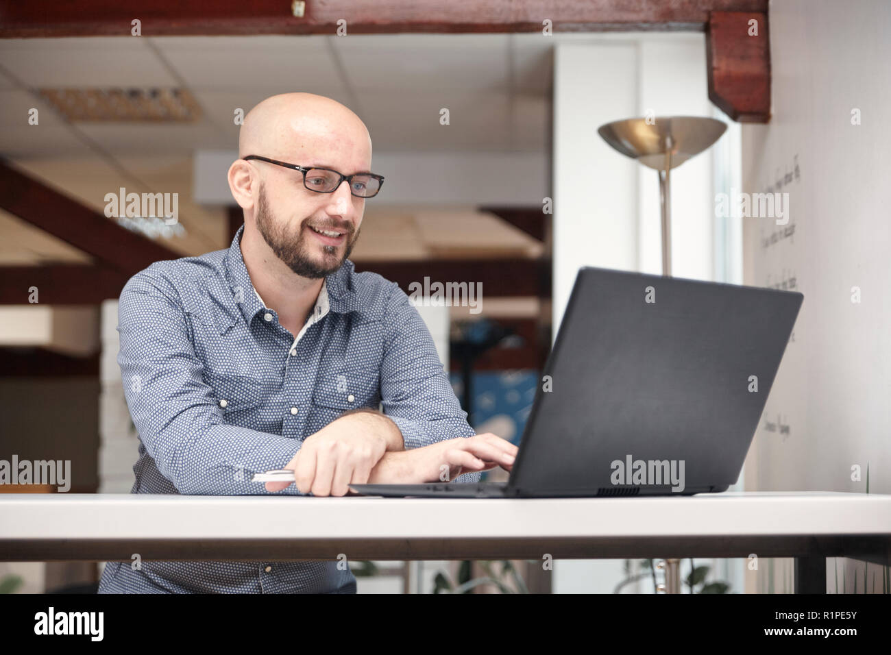 Un uomo, 30-39 anni, utilizzando laptop in un ufficio moderno interno. luminose. Foto Stock