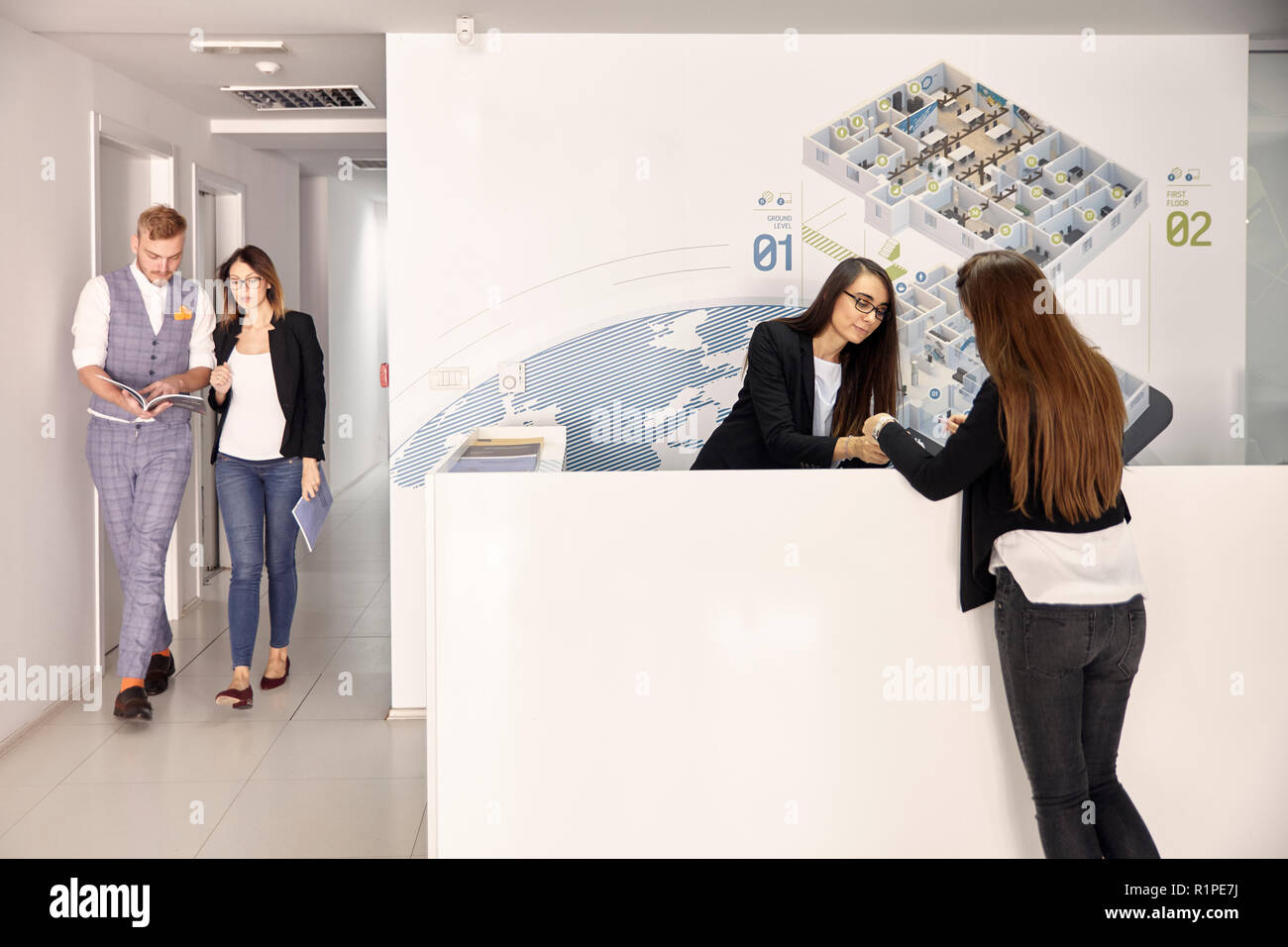 Gruppo di persone, due persone a piedi, due donne alla ricerca di documenti in un ufficio moderno corridoio. Foto Stock