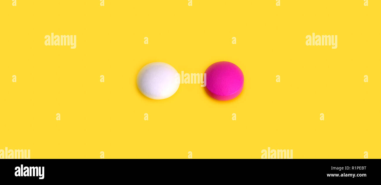Due pillole rosa e bianco su sfondo giallo. Foto Stock