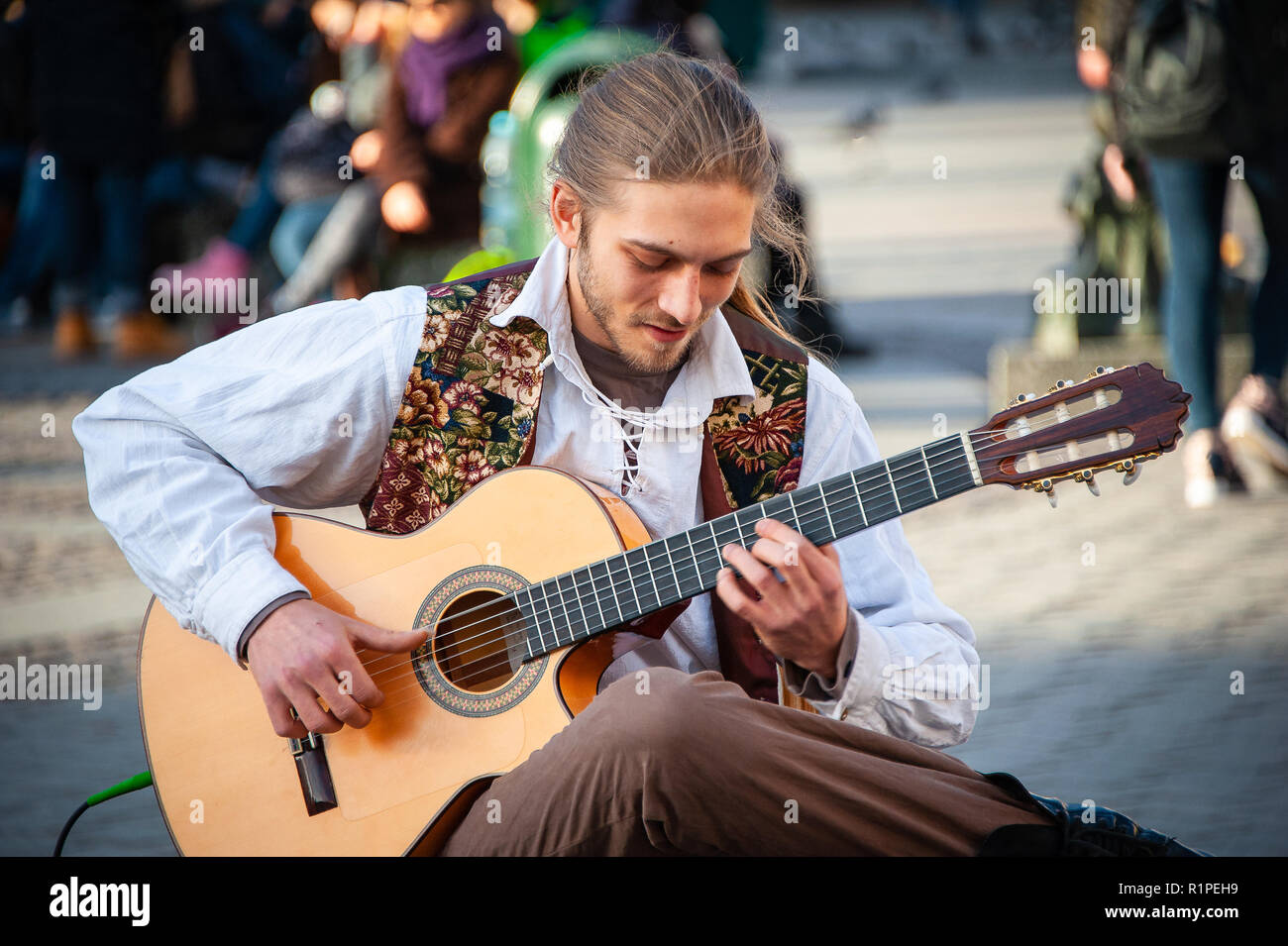 Cracovia in Polonia: un suonatore ambulante suona la chitarra nella piazza del vecchio mercato. Sorridente, seduto musicista esegue su una chitarra acustica ad una folla di persone. Foto Stock