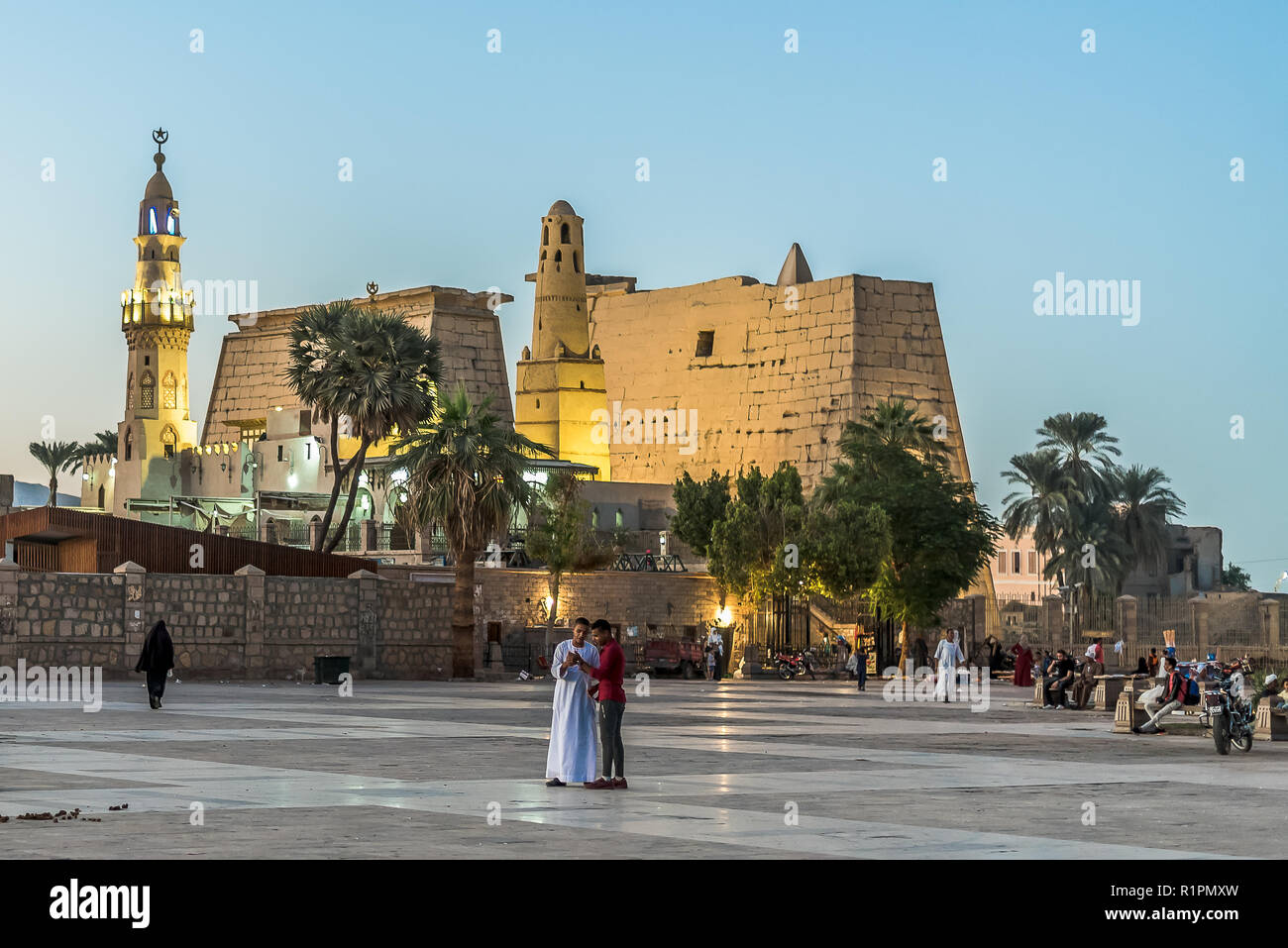 Le persone in piedi in piazza con i loro telefoni cellulari nella parte anteriore dell'illuminato Tempio di Luxor e di notte con il cielo blu e incandescente brickwalls vecchia, Luxor Foto Stock