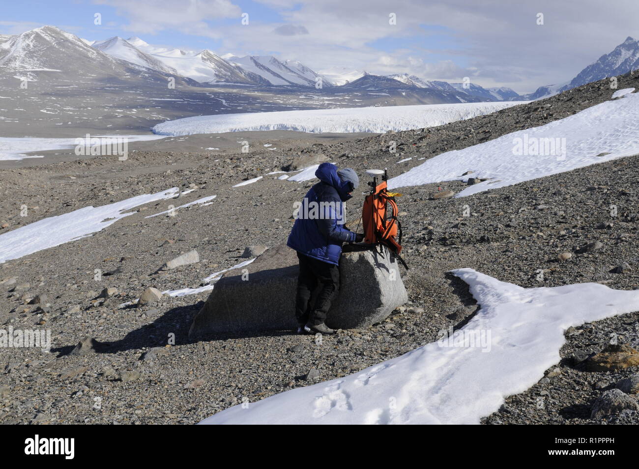 Scienziato la registrazione dei dati GPS in Taylor Valley, McMurdo aride vallate, Antartide, con il lago Fryxell e Canada ghiacciaio in background Foto Stock