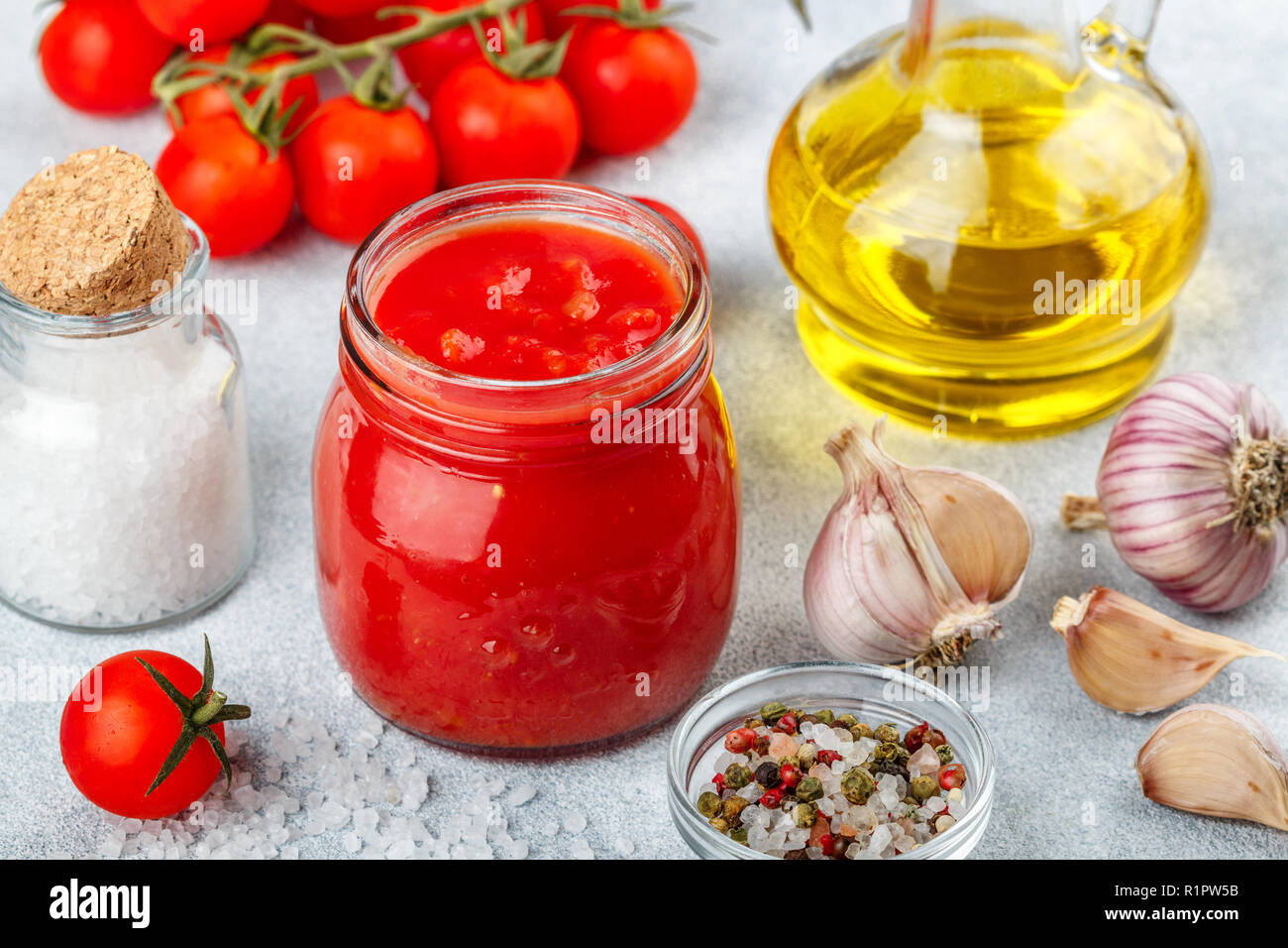Tradizionale salsa di pomodoro in un vasetto di vetro con aglio e spezie. Ingredienti e olio d'oliva sulla superficie della luce. Messa a fuoco selettiva Foto Stock