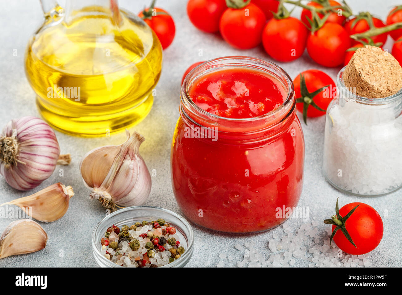 Tradizionale salsa di pomodoro in un vasetto di vetro con aglio e spezie. Ingredienti e olio d'oliva sulla superficie della luce. Messa a fuoco selettiva Foto Stock