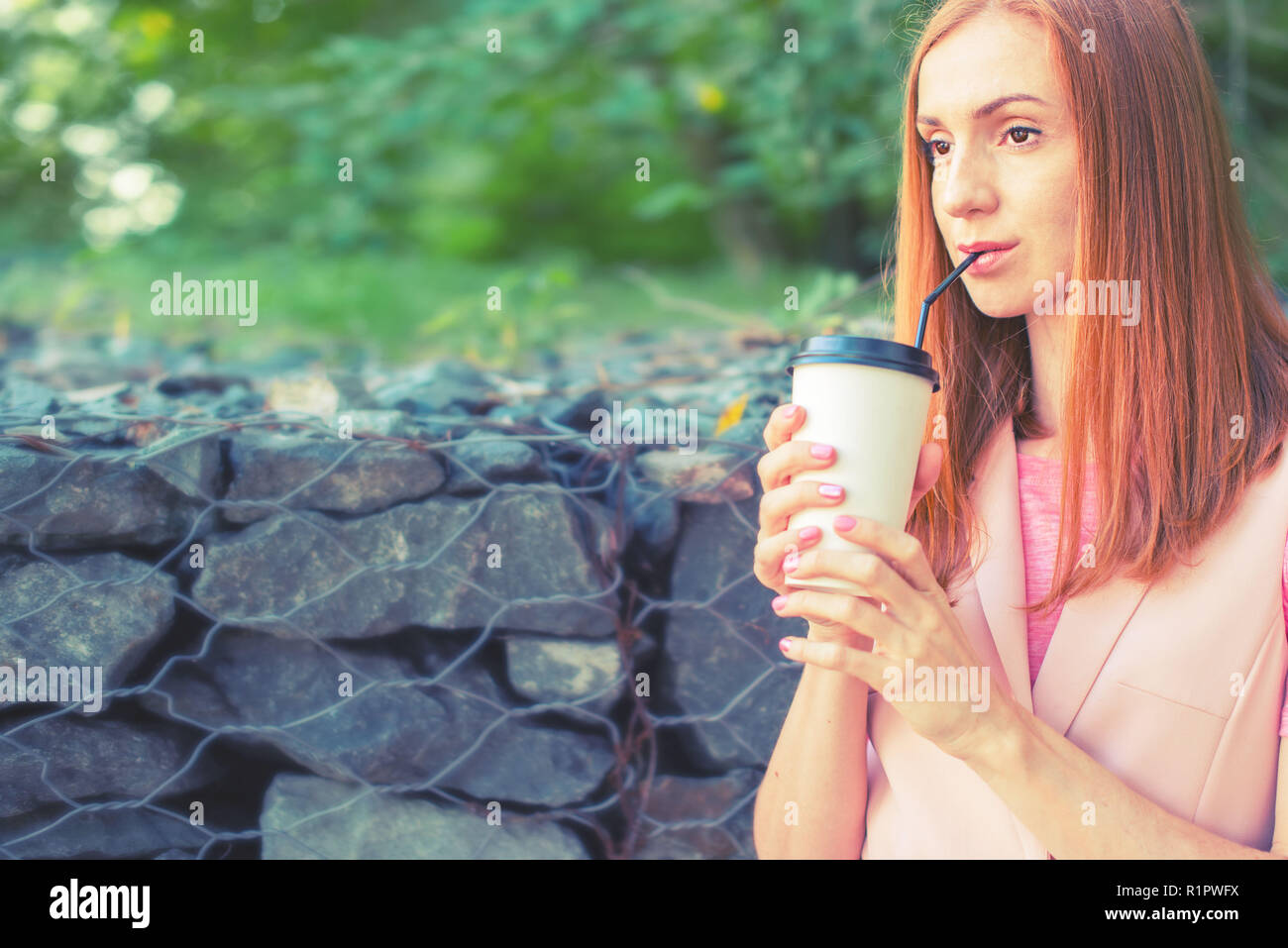 Una bella i Capelli rossi ragazza va giù per le scale e beve caffè da un bicchiere di carta. La prima colazione di stile di vita nel parco Foto Stock