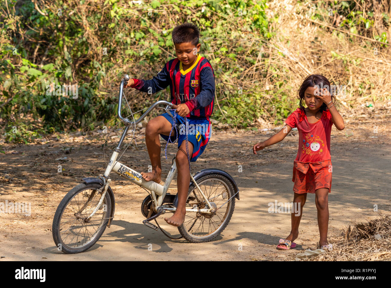 Don Det, Laos - Aprile 22, 2018: Ragazza aiutando un ragazzo a guidare una bicicletta su un percorso in un remoto villaggio del sud Laos Foto Stock