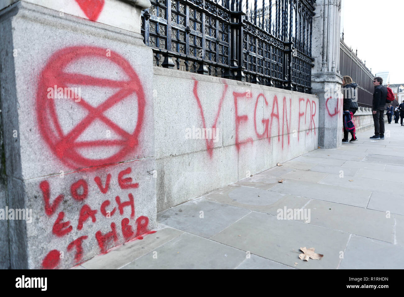 Londra, Regno Unito. 14 novembre 2018. Graffiti dipinti a spruzzo rosso con la scritta “VEGAN FOR CLIME?” su un muro di pietra all'esterno di un edificio pubblico, possibilmente governativo o storico. Accompagnato da marcature simboliche, tra cui un motivo a clessidra nel cerchio. Ambiente urbano con alberi ed edifici sullo sfondo. Suggerisce protesta o sostegno in relazione al cambiamento climatico e al veganismo. Graffiti spruzzati sulle pareti che circondano le camere del Parlamento dal gruppo ambientalista Extinction Rebellion. Penelope Barritt/Alamy Live News Foto Stock