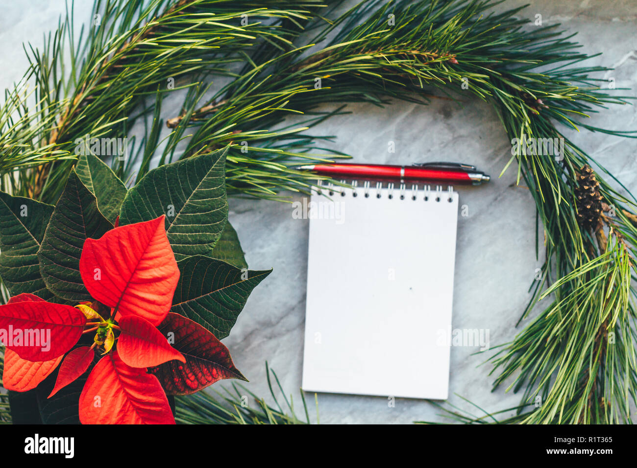 Natale closeup mockup con poinsettia, ghirlanda di pino, notebook, con copia posto. Sfondo accogliente Foto Stock