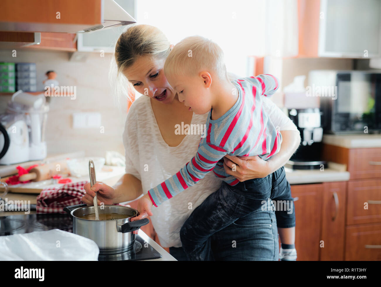 Un disabili affetti da sindrome di down boy cottura della zuppa con sua madre in ambienti chiusi. Foto Stock