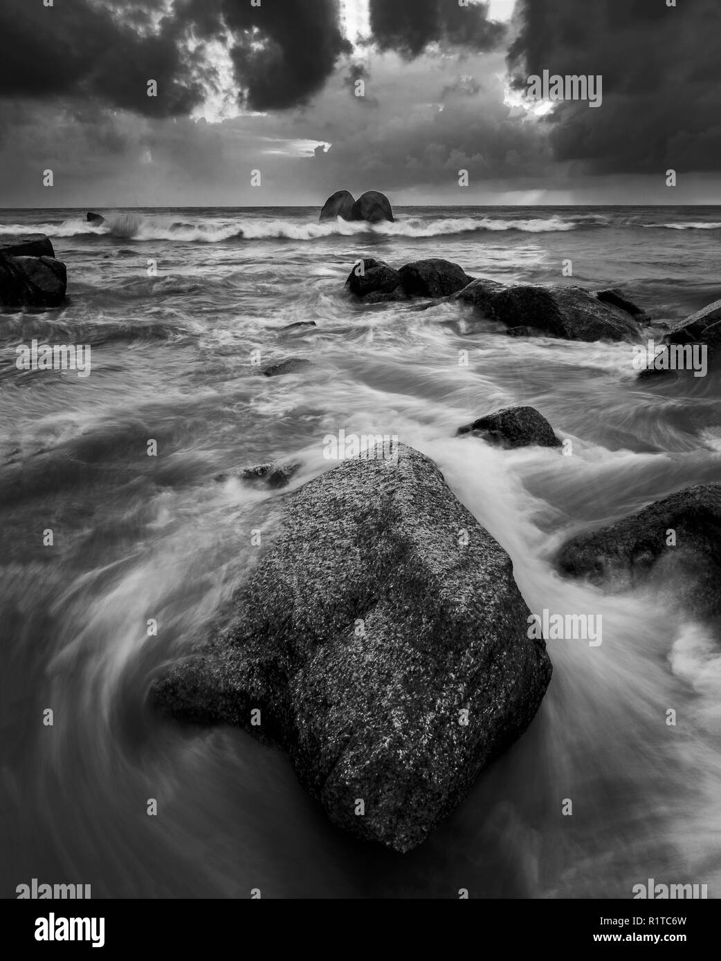 Ruvida continuamente le onde si infrangono le rocce in spiaggia durante la stagione dei monsoni appena prima che la pioggia inizia a versare in basso Foto Stock