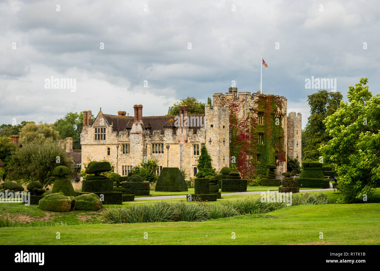 Il castello di Hever, England, Regno Unito - 08 settembre 2018: Vista di Hever Castle e la sua topiaria da giardino in una giornata nuvolosa con una bandiera a pieno il montante. Foto Stock