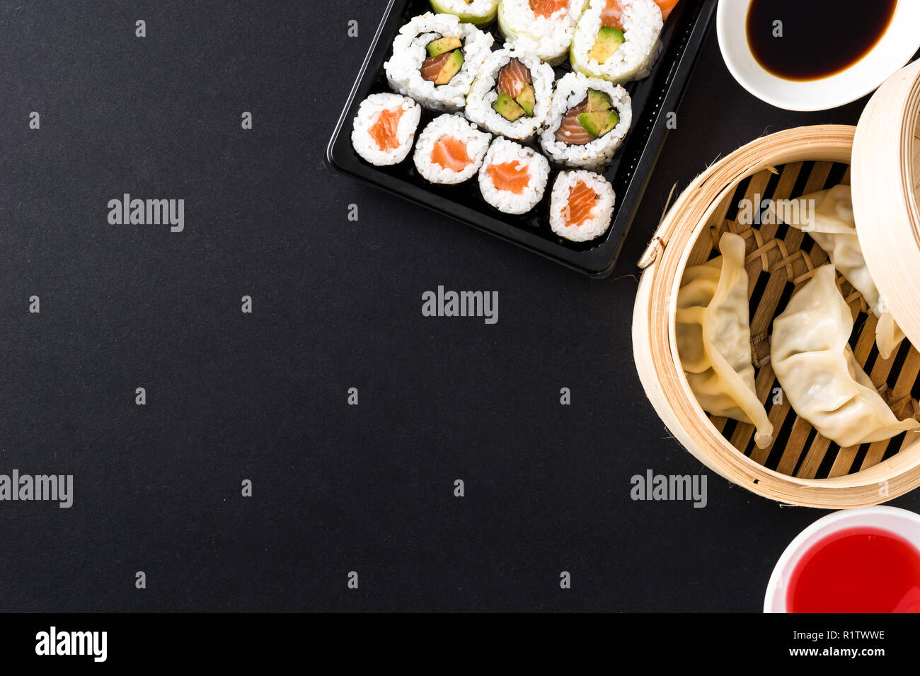 Canederli o gyoza serviti nel tradizionale sistema di cottura a vapore e sushi su sfondo nero. Vista dall'alto. Copyspace Foto Stock