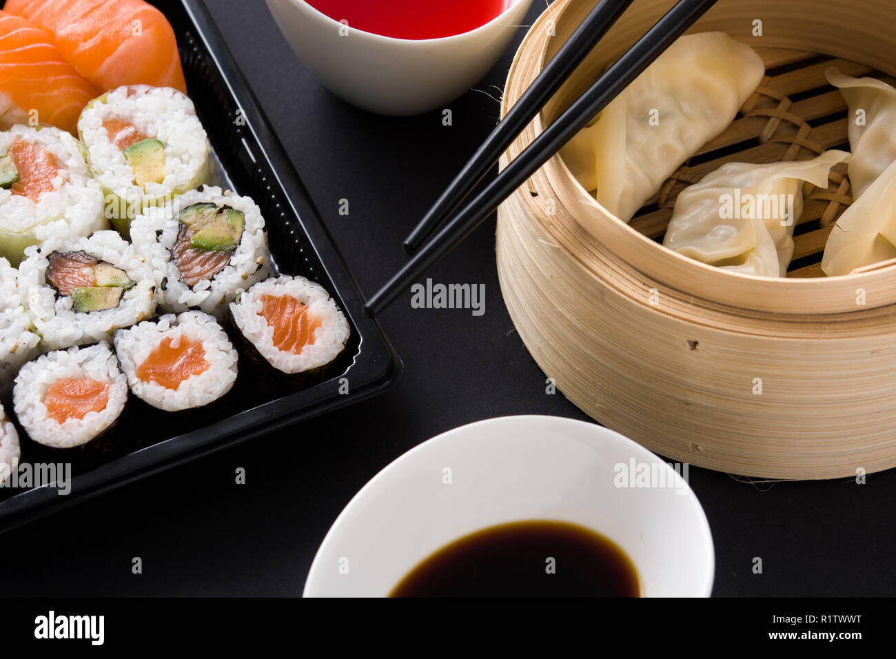 Canederli o gyoza serviti nel tradizionale sistema di cottura a vapore e sushi su sfondo nero. Close up Foto Stock