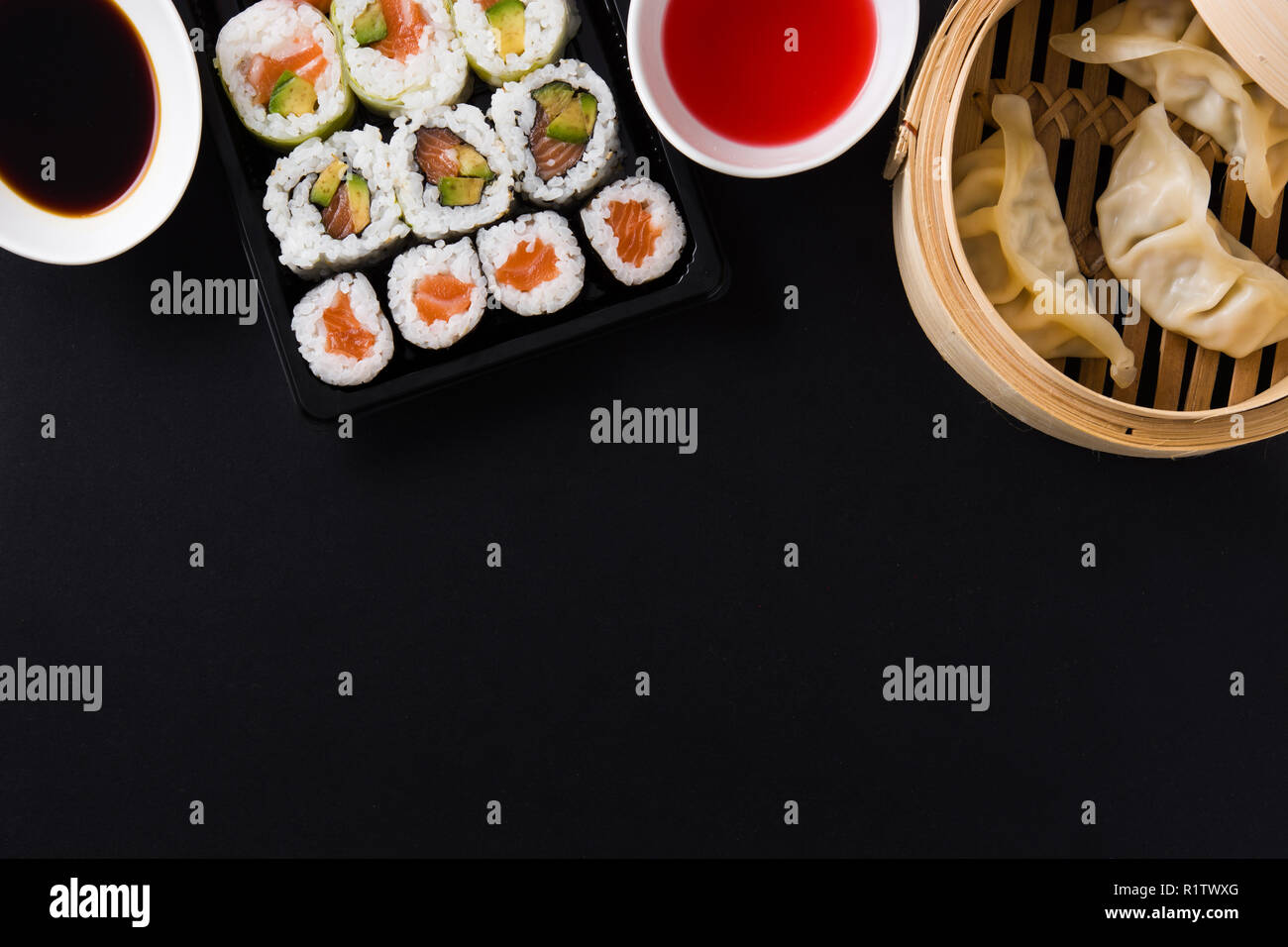 Canederli o gyoza serviti nel tradizionale sistema di cottura a vapore e sushi su sfondo nero. Vista dall'alto. Copyspace Foto Stock
