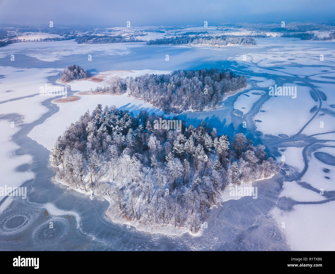 Vista aerea della neve invernale coperto foresta e lago ghiacciato dal di sopra catturato con un drone in Lituania. Foto Stock