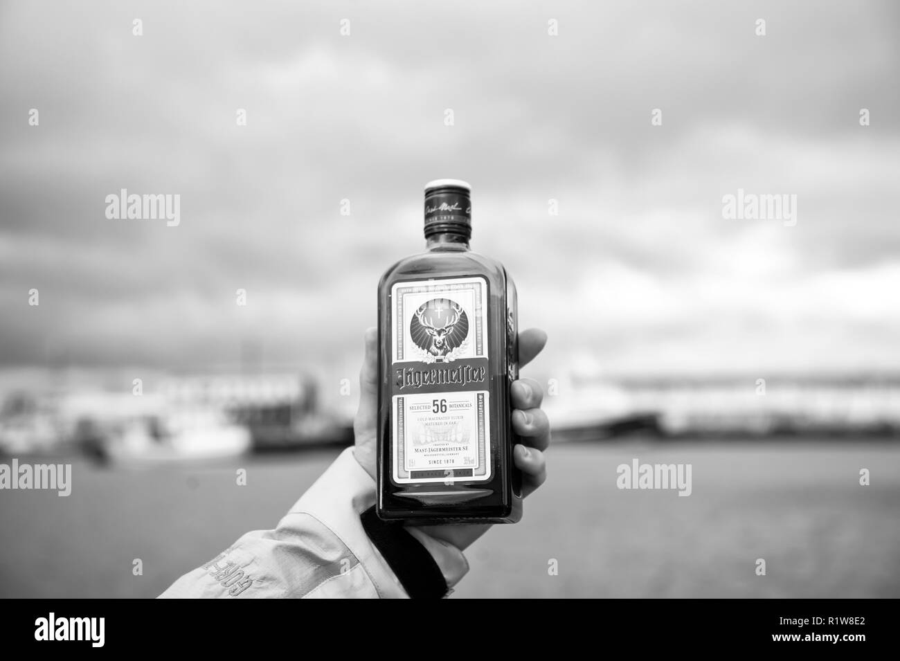 Reykjavik, Islanda - 13 Ottobre 2017: bottiglia di Jagermeister in mano sul mar. Bere alcool con erbe e spezie sul cielo nuvoloso. Le cattive abitudini e la tossicodipendenza. Bere outdoor durante il rilassarsi e godere. Foto Stock