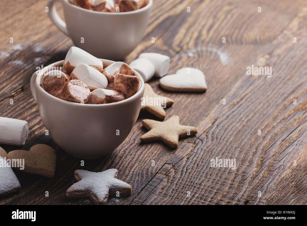 Piastra di biscotti di Natale spolverati con zucchero a velo e tazze di cioccolata calda con marshmallows sul tavolo di legno Foto Stock