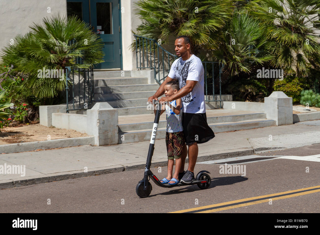 Adulto e bambino a cavallo di un "Bird" scooter elettrico su un sentiero a San Diego, California, Stati Uniti. Foto Stock