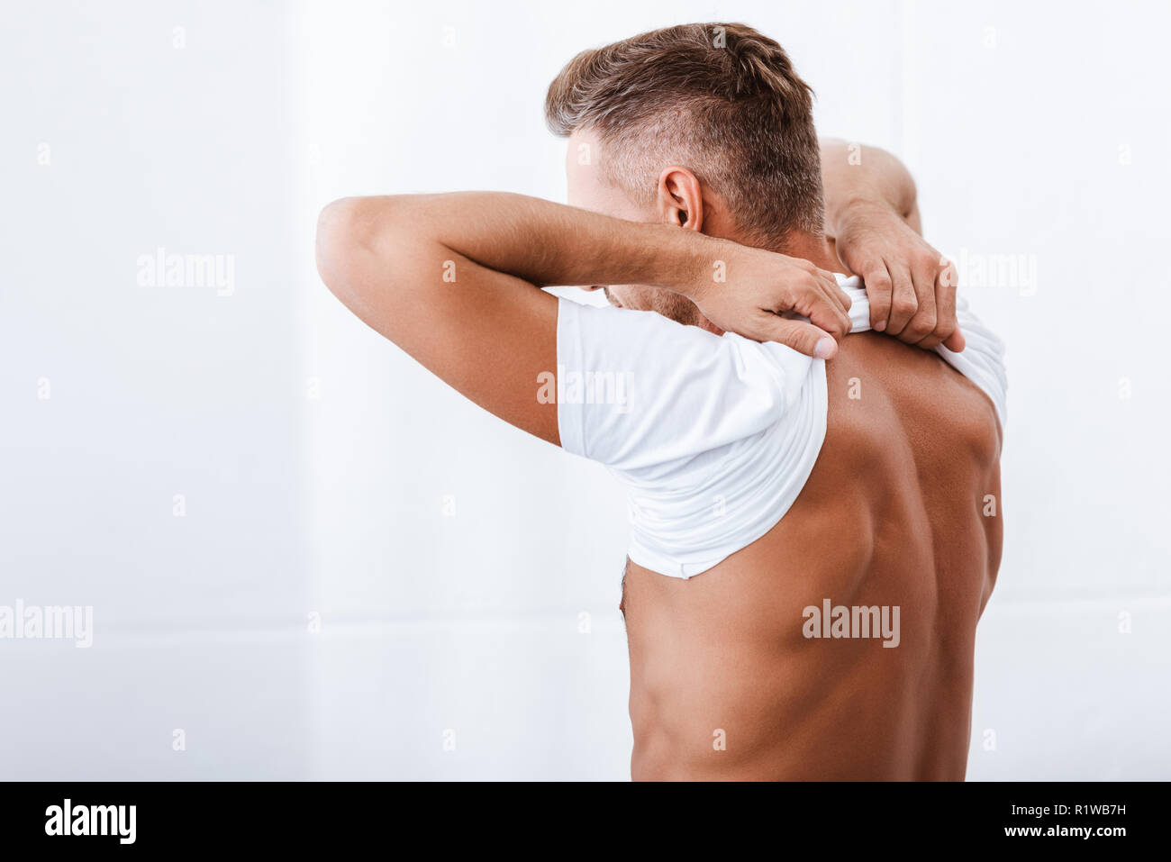 Vista posteriore di uomo adulto mettendo su t-shirt bianco durante la mattina tempo a casa Foto Stock
