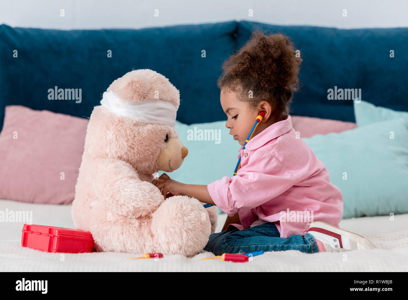 Poco americano africano bambino in camicia rosa la riproduzione del medico con Teddy bear Foto Stock