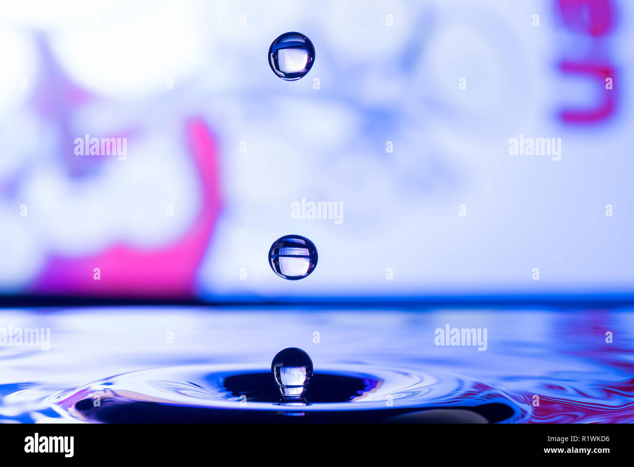 Le goccioline di acqua caduta in acqua con sfondo colorato Foto Stock
