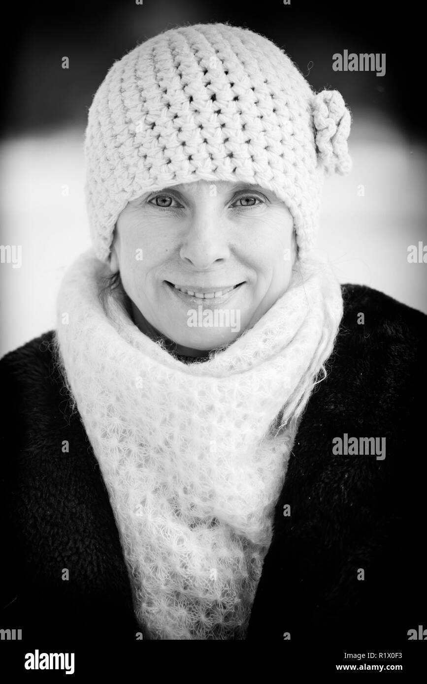 Un inverno ritratto di un sorridente senior adulto donna che indossa un cappello di lana e una sciarpa con un background di neve Foto Stock