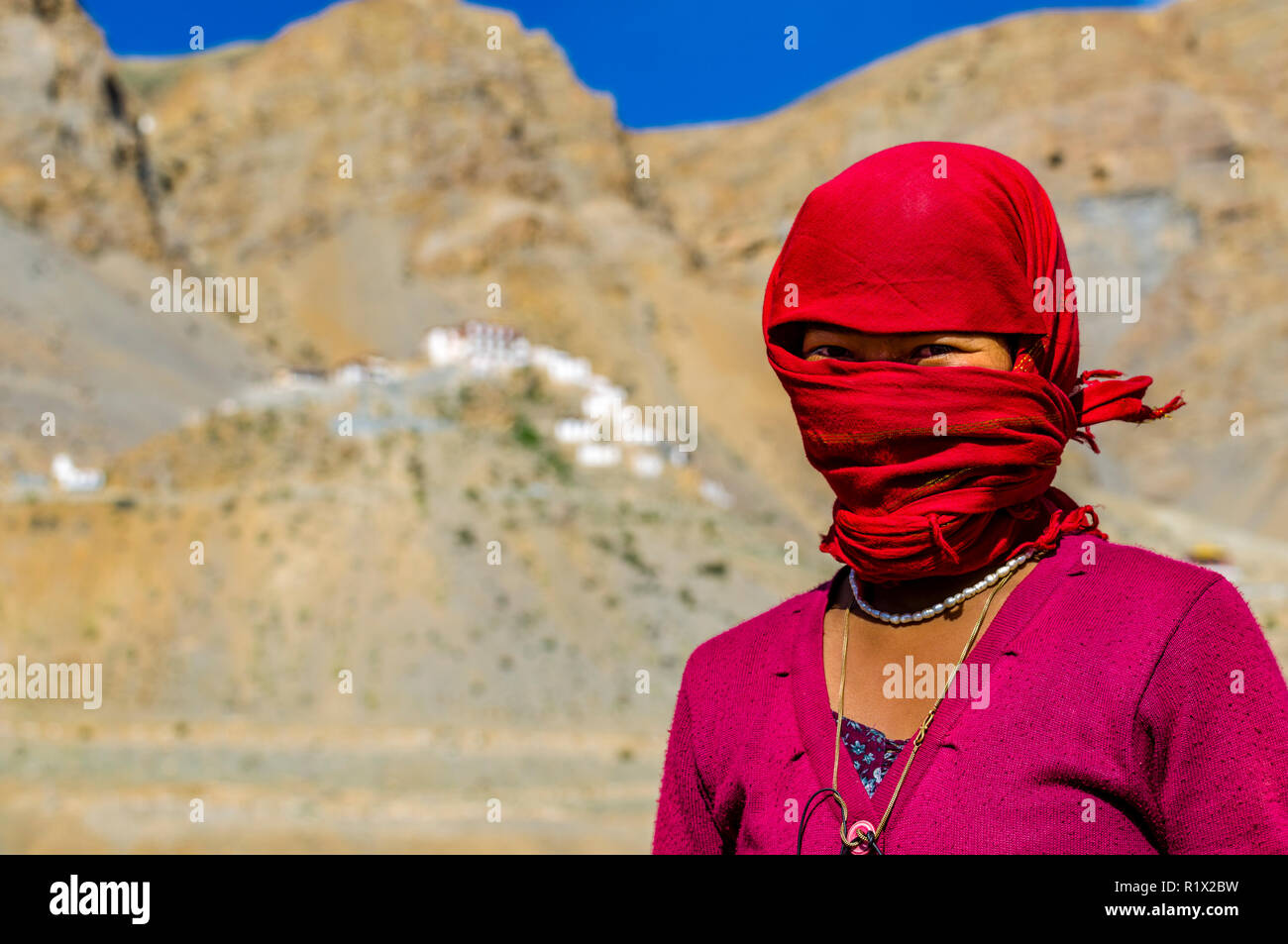 Un ritratto di una donna locale lavora su un campo in alta quota della Spiti Valley, che copre il volto dalla polvere da tessuto tessuto rosso Foto Stock