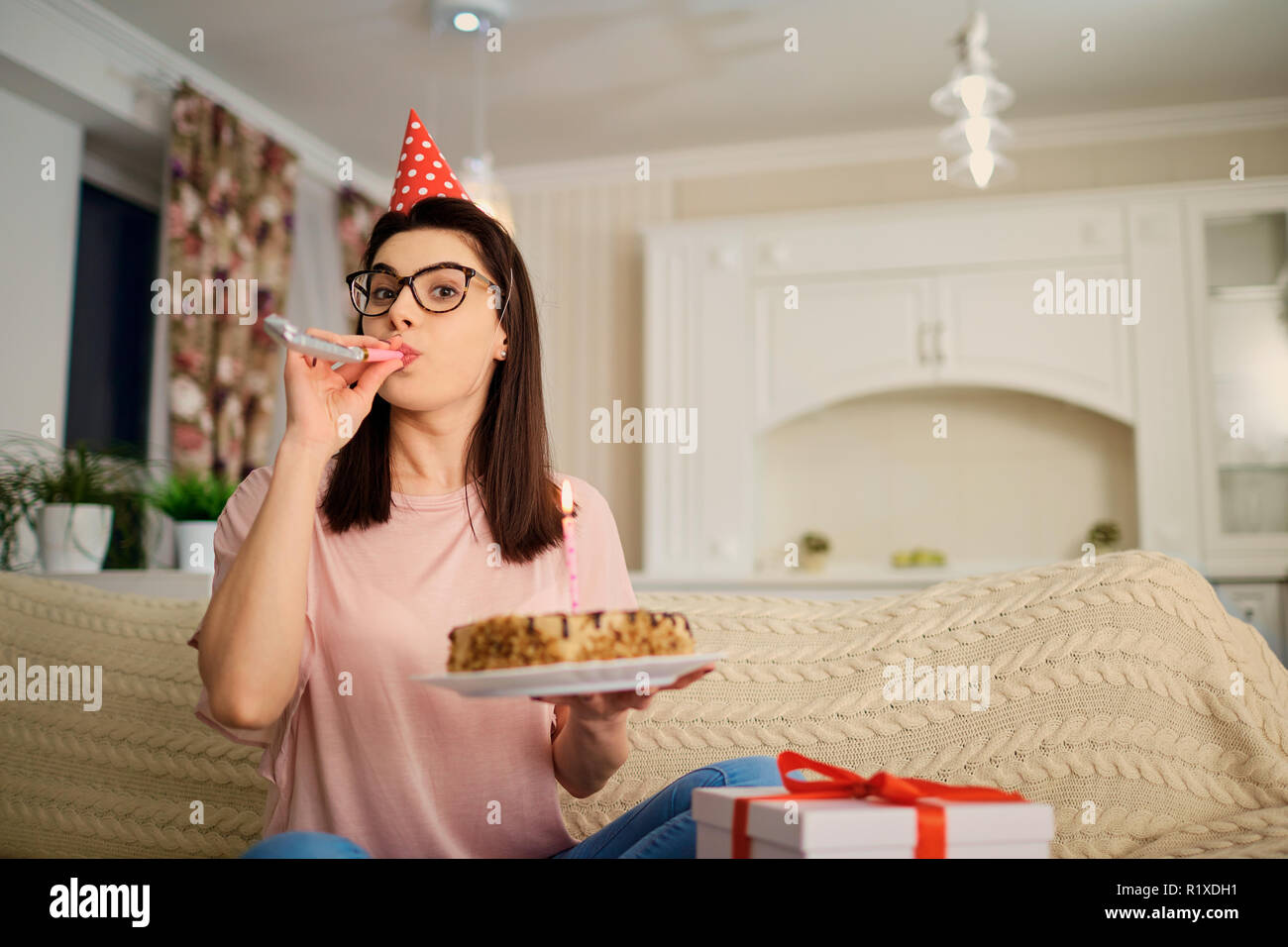 Una ragazza in un tappo da solo con una torta con candele in camera. Foto Stock