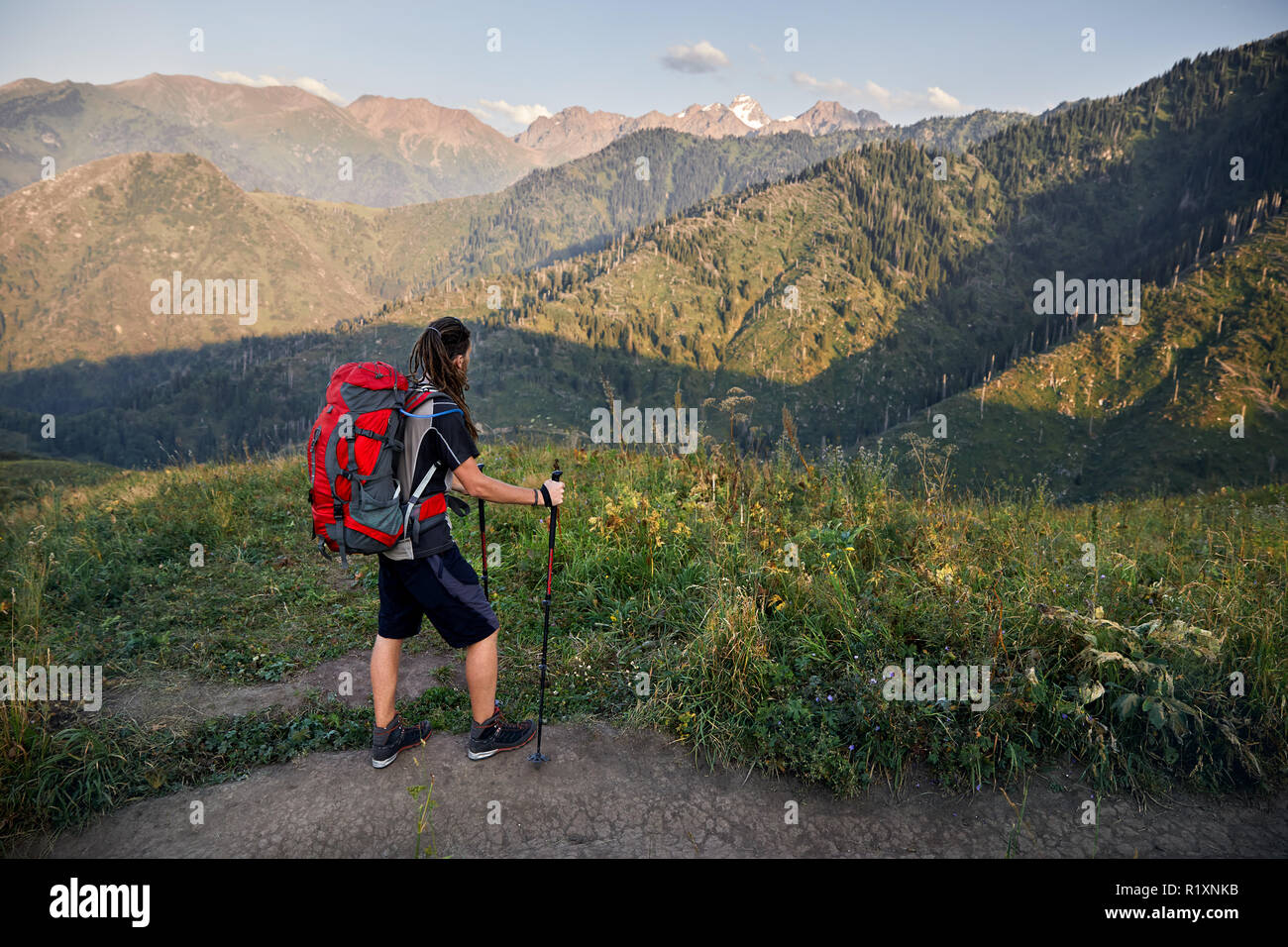 Uomo con dreadlocks e zaino rosso in montagna in Cielo di tramonto sullo sfondo Foto Stock