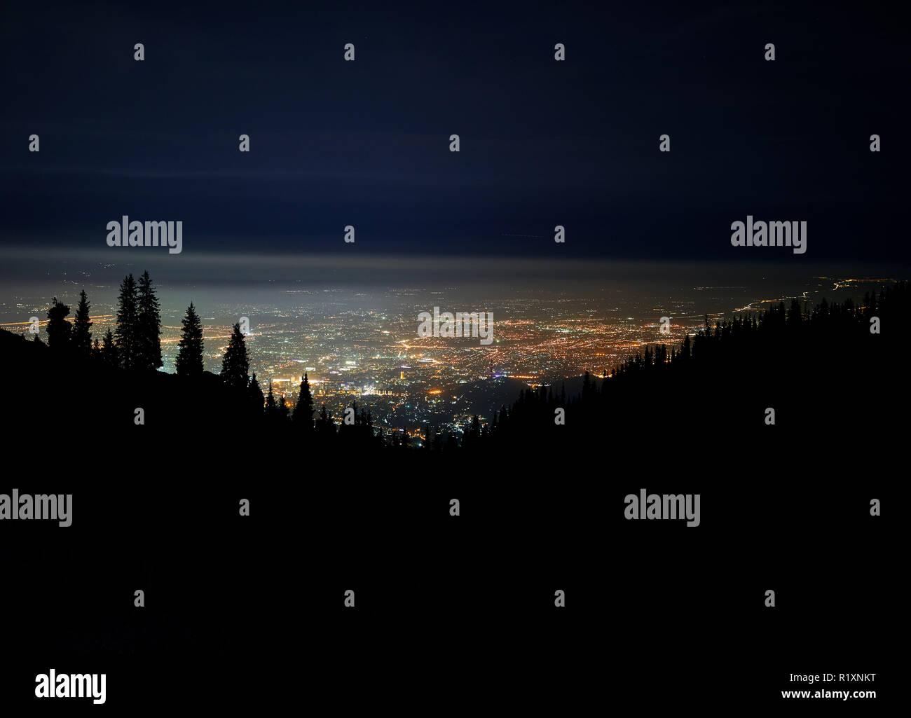 Incandescente luci della città di notte il cielo con le stelle e sagome di pino e montagna in Almaty, Kazakhstan. Foto Stock