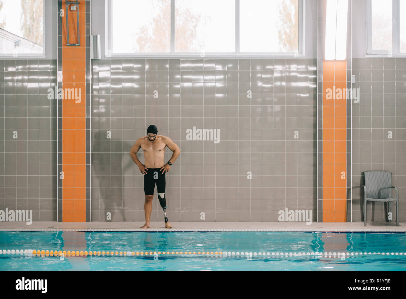 Muscoloso giovane sportivo con gamba artificiale in piedi sul bordo della piscina a piscina interna Foto Stock