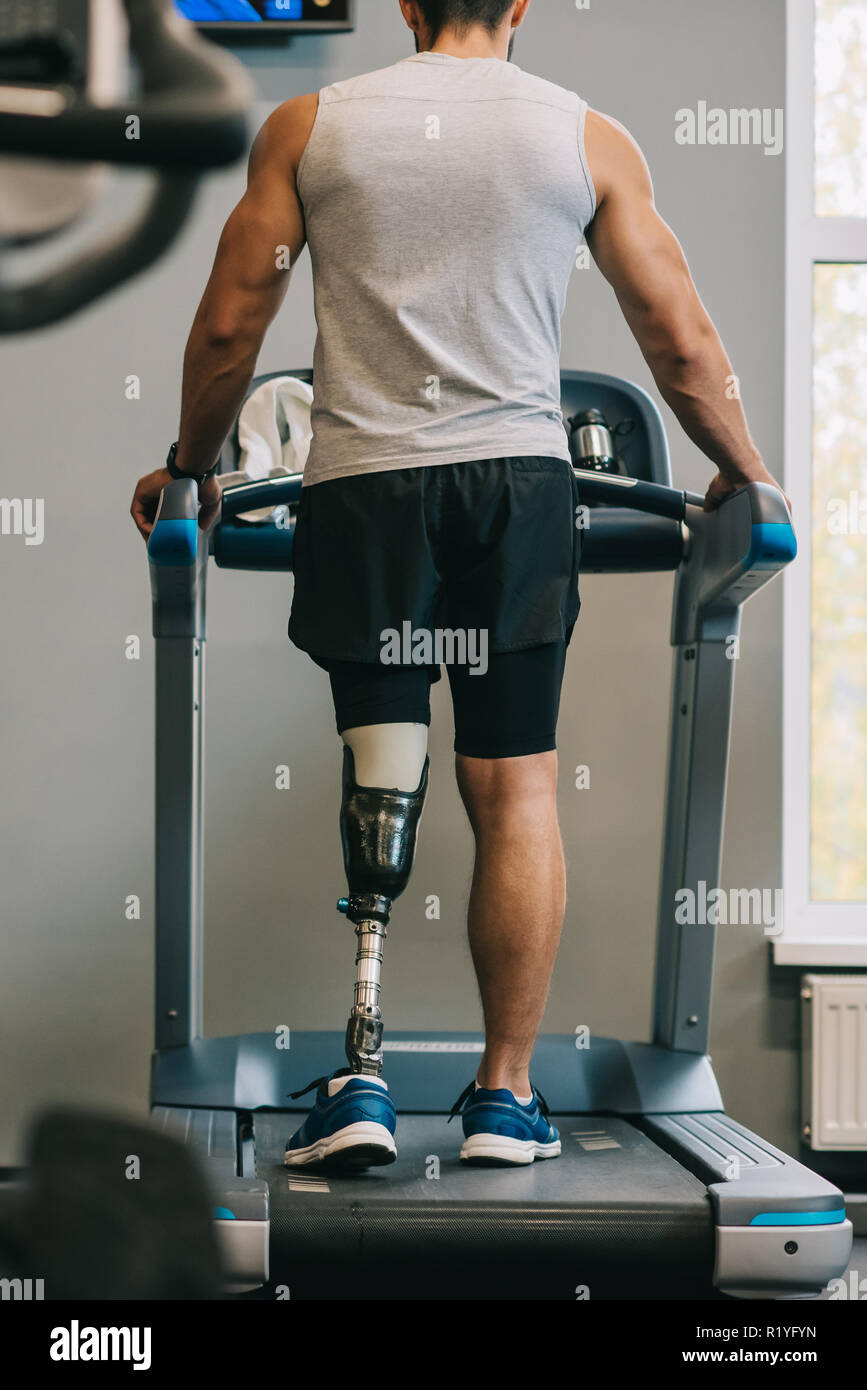 Vista posteriore del giovane sportivo con gamba artificiale camminando sul tapis roulant in palestra Foto Stock