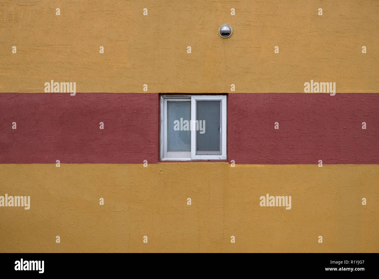 Unica piccola finestra quadrata con cornice bianca e una minima striscia rossa sulla parete gialla abstract Foto Stock
