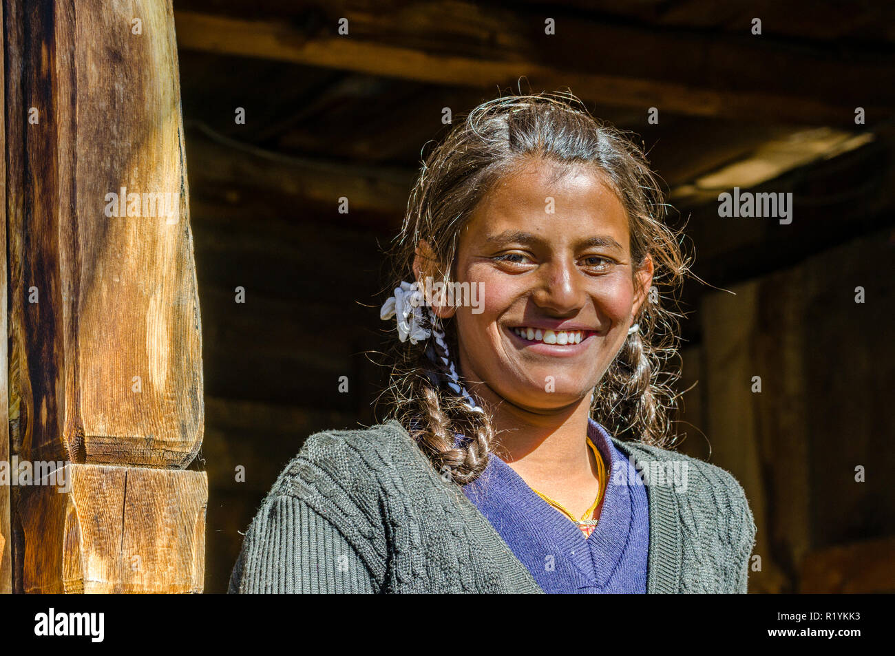 Una ragazza locale a sorridere di fronte a una casa in legno in Chitkul, l'ultimo villaggio della valle di Sangla Hill, situato a 3.400 m e circondato dalla coperta di neve mounta Foto Stock