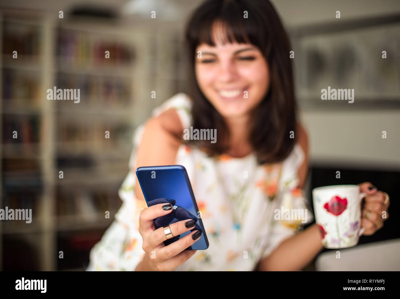 Giovani allegro sorridente brunette donna video chat con l'amico, alla ricerca di un nuovo smartphone durante permanente di messa a fuoco interna sullo smartphone Foto Stock