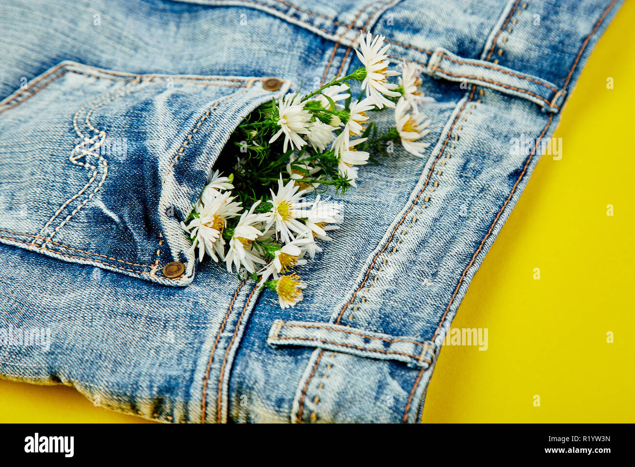 Bouquet di fiori bianchi nella tasca di un paio di jeans su sfondo giallo.  Minimalista. Concetto di denim. Lay piatto. Copia dello spazio. Layout  creativi per la primavera fest Foto stock -