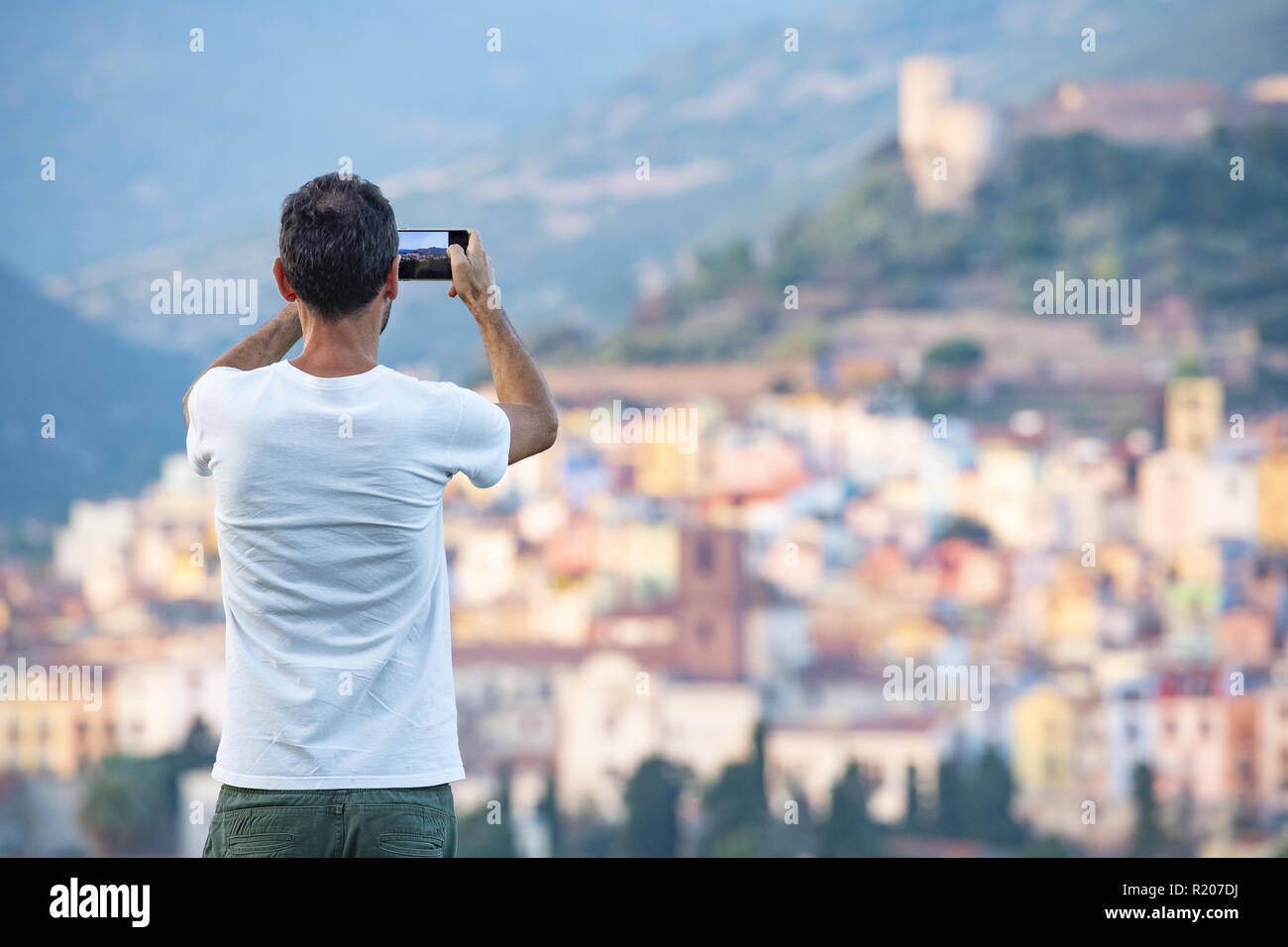 Un turista è di scattare una foto con il suo telefono cellulare al bello e colorato villaggio di Bosa si trova nel nord-ovest della Sardegna, Italia. Foto Stock