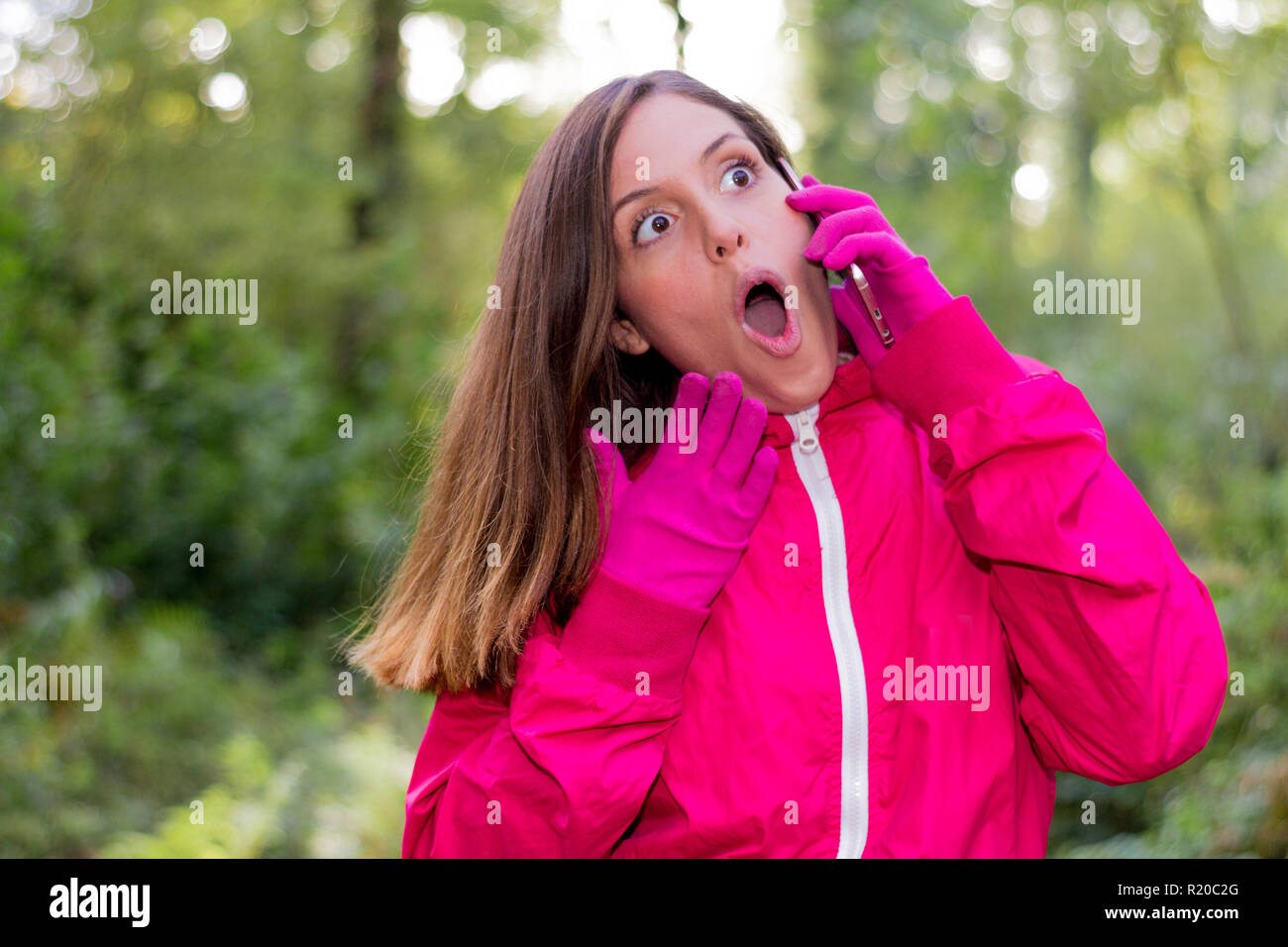 Sorpreso bruna giovane donna con la bocca aperta avvolto all'aperto parlando al telefono cellulare molto espressiva nel suo tempo di ricambio Foto Stock