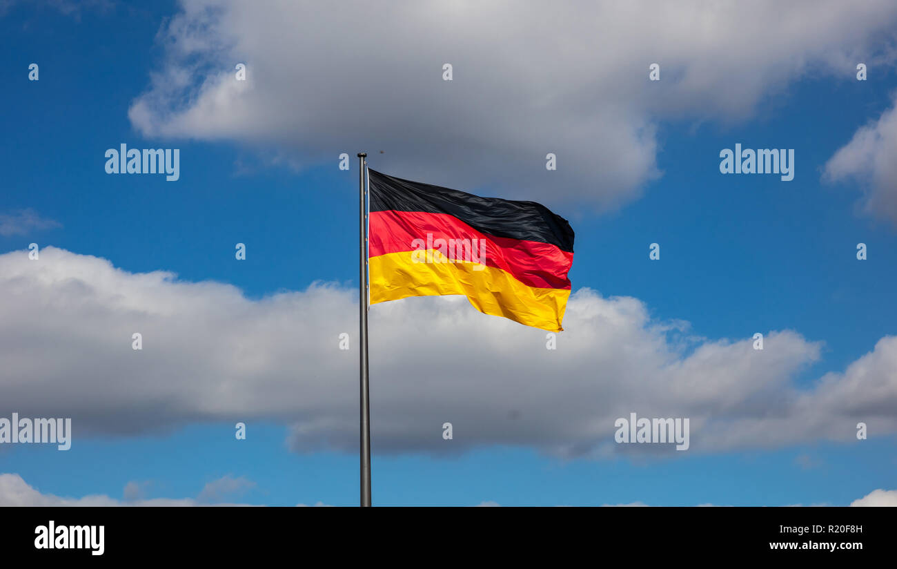 Bandiera tedesca sventola su un pennone contro il cielo blu con nuvole, la carta da parati. Foto Stock