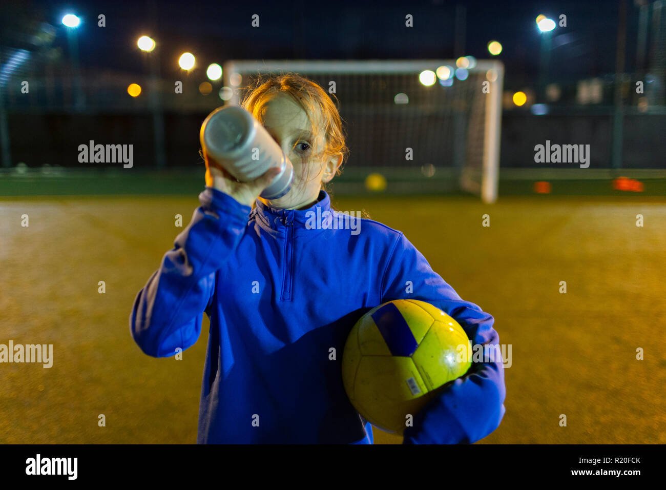 Ragazza giocatore di calcio di prendere una pausa, acqua potabile sul campo di notte Foto Stock